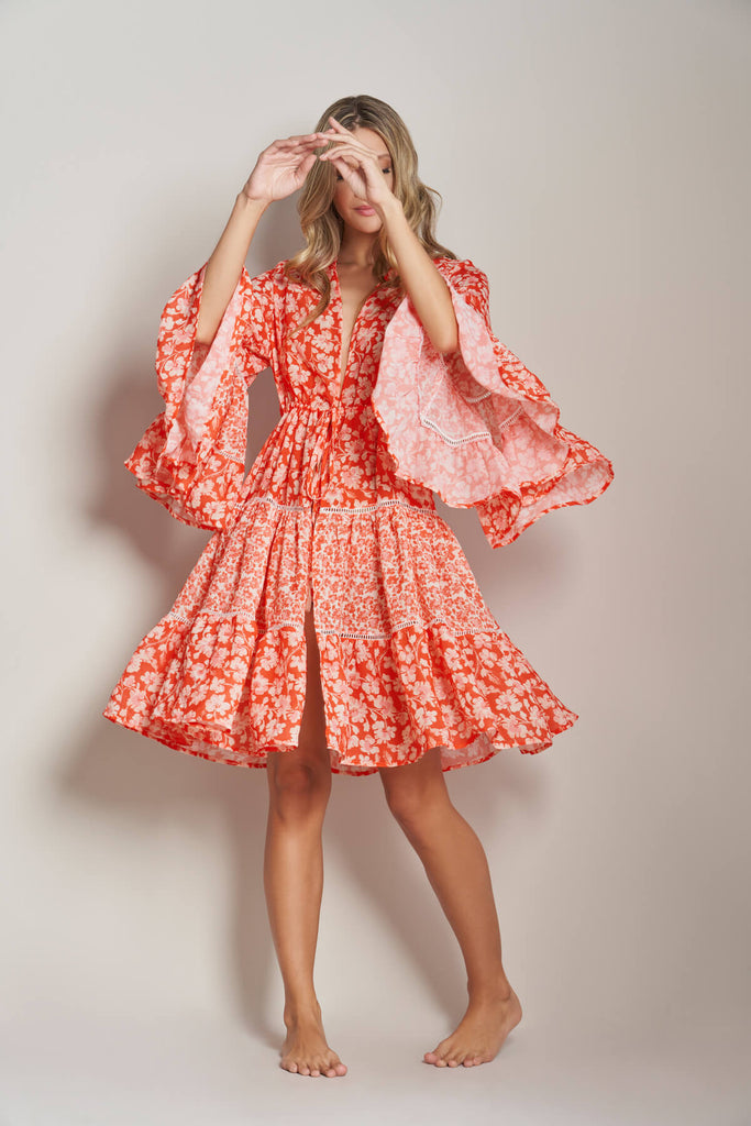 A model standing and swirling the Floral Short Beach Kimono, a short dress with bell sleeve and a tie on the front and handmade decorative crochet stitch.